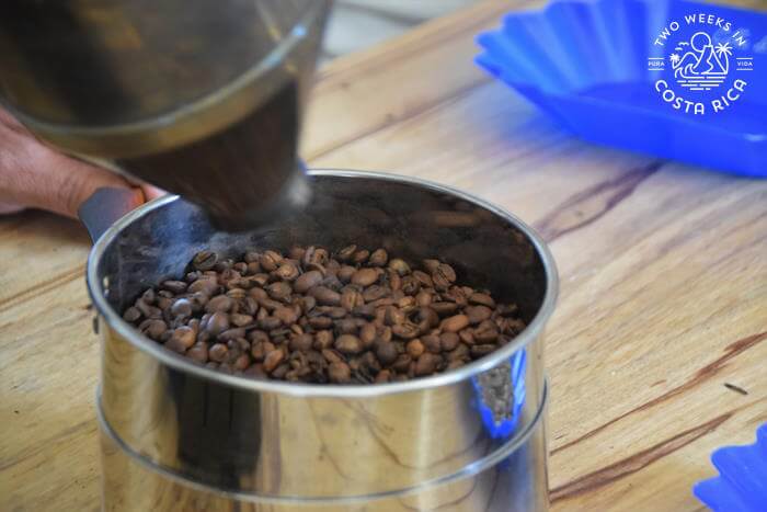 Silver roasting canister holding dark brown coffee beans