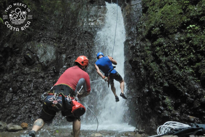 guide helping someone rappel down a large waterfall