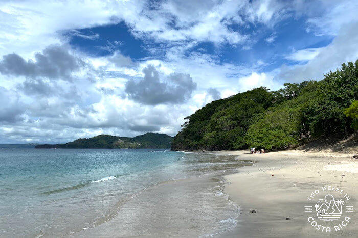 Sandy beach with blue water and lush greenery